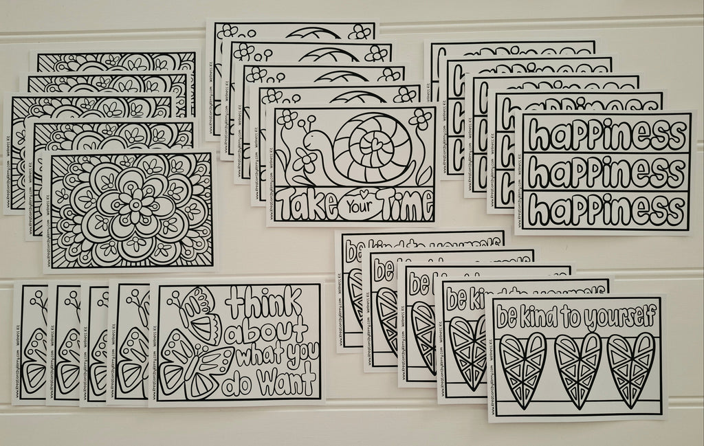 A set of black and white printable coloring pages and art cards arranged on a light beige wall. The designs include floral mandalas, butterflies, hearts, and motivational quotes such as 'happiness happiness' and 'think about what you do want.